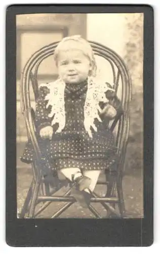 Fotografie unbekannter Fotograf und Ort, Kleines Mädchen im gepunkteten Kleid mit Rüschenkragen auf einem Stuhl
