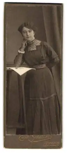 Fotografie Emil Schröter, Jüterbog-Luckenwalde, Trebbinerstr. 6, Junge Frau im taillierten Kleid an einem Beistelltisch
