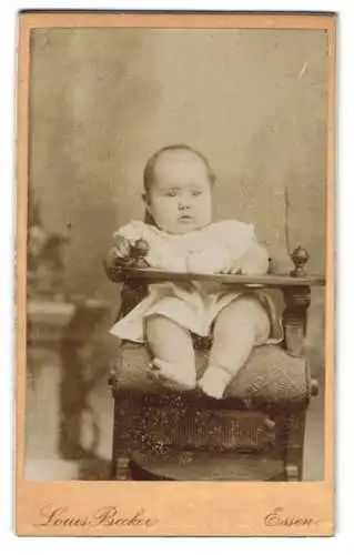 Fotografie Louis Becker, Essen, Einhornstrasse 3, Kleinkind im weissen Gewand auf einem Babystuhl, mit fragendem Blick