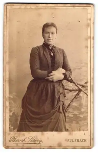 Fotografie Bernh. Schery, Sulzbach, Junge Dame im dunklen Kleid mit schwarzer Bluse darunter, mit dezenter Kette