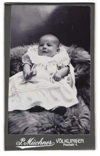 Fotografie P. München, Völklingen, Poststr. 1, Baby im weiten, weissen Gewand auf einem dicken Pelz