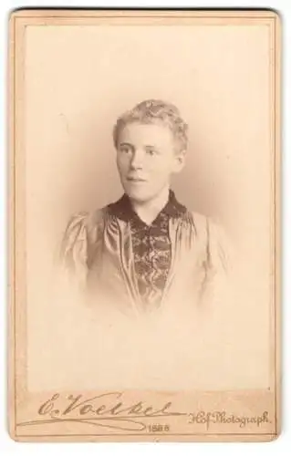 Fotografie E. Voelkel, Neisse, Ring 18, Junge Dame mit lockigem Haar und schwarzer Zierbluse unterm Kleid