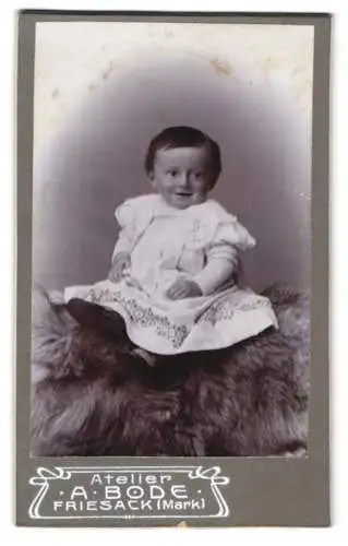 Fotografie A. Bode, Friesack (Mark), Kleinkind im weissen verzierten Kleid mit einem Lächeln im Gesicht