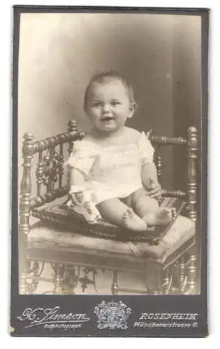 Fotografie X. Simson, Rosenheim, Münchenerstrasse 6, Lachendes Kleinkind im weissen Gewand auf einem Kissen