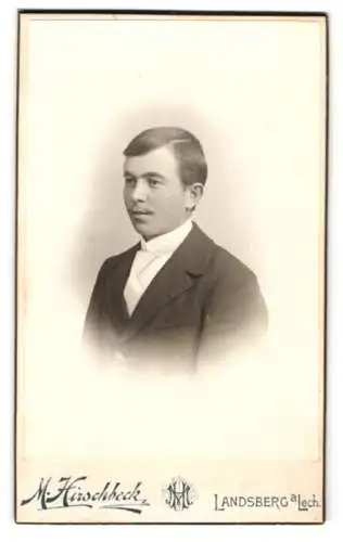 Fotografie M. Hirschbeck, Landsberg a. Lech, Jugendlicher Knabe im Anzug mit weisser Krawatte, mit leichtem Schnäuzer