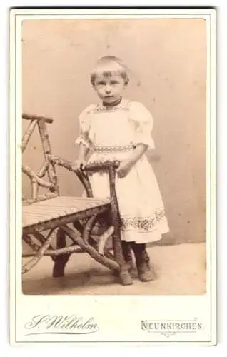 Fotografie S. Wilhelm, Neunkirchen, Bahnhofstrasse, Kleines Mädchen mit kurzem Haar im weissen Kleid mit Zierbändern