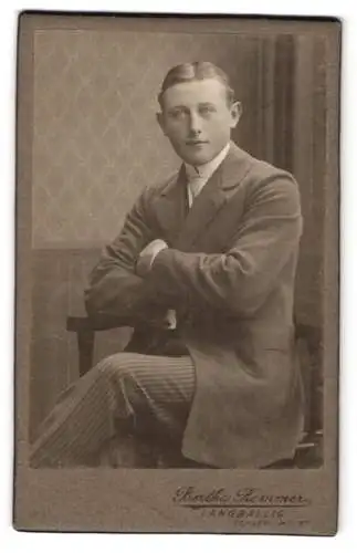 Fotografie Bertha Remmer, Langballig, Junger Mann mit Mittelscheitel und gestreifter Hose auf einem Stuhl