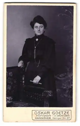 Fotografie Oskar Goetze, Hannover, Heiliger-Str. 3, Schöne junge Dame im schwarzen Kleid mit langer Brosche und Buch