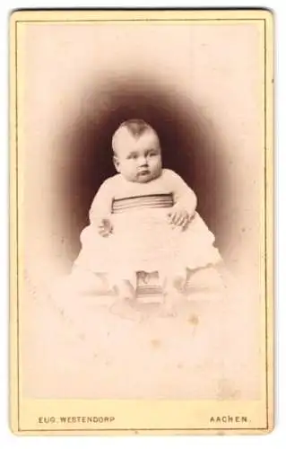 Fotografie Eug. Westendorp, Aachen, Damengraben 19, Niedliches Baby im weissen Kleid mit Mittelhaarfrisur