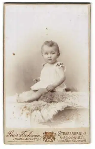 Fotografie Louis Frohwein, Strassburg, Gutenbergplatz 7, Niedliches Baby im weissen Kleid mit Schleifen und kurzem Haar