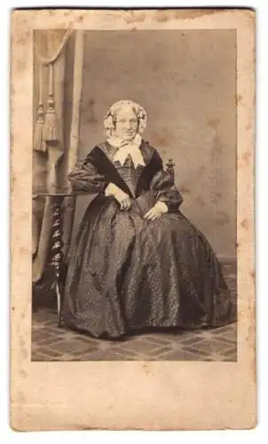 Fotografie E. Bieber, Hamburg, Portrait älter Dame im Kleid mit Haube posiert sitzend im Atelier