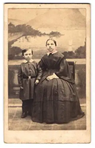 Fotografie B. Sparmeyer, Herrnhut, Mutter im dunklen Kleid mit Haube nebst ihrem Sohn vor einer Studiokulisse
