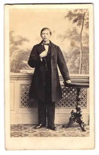 Fotografie Stiehm, Berlin, Jäger-Str. 42, junger Mann im dunklen Anzug mit Mantel und Fliege vor einer Studiokulisse