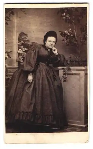 Fotografie Julius Menzel, Ort unbekannt, korpulente Dame im dunklen Kleid lehnt an einem Podest
