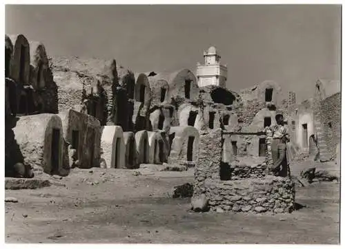 Fotografie unbekannter Fotograf, Ansicht Tunesien, Brunnen inmitten von Wohnhöhlen, Turm einer Moschee