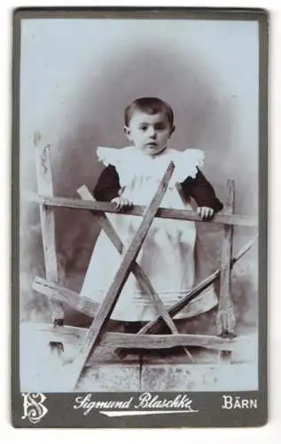 Fotografie Sigmund Blaschke, Bärn, Kleines Kind im Kleid steht am Zaun