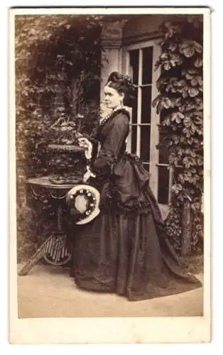Fotografie W. Wort, Birmingham-Oscott, attraktive junge Engländerin im dunklen Kleid mit Hut vor einer Studiokulisse