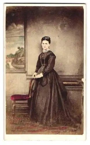 Fotografie T. W. Thompson, London, hübsche junge Dame im dunklen Kleid vor einer Studiokulisse, Handkoloriert