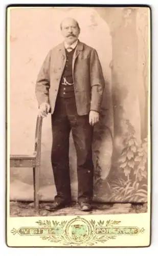 Fotografie Atelier E. J. Kabát, Ort unbekannt, Bürgerlicher Herr mit Halbglatze und einem Schnurrbart, stehend