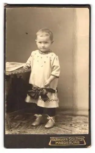 Fotografie Hermann Schlüter, Magdeburg, Kleinkind im weissen Kleid mit grosser schwarzer Schleife