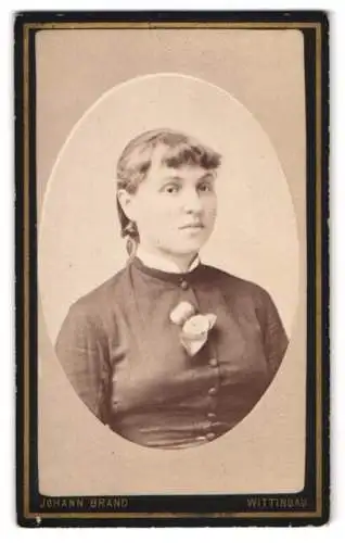 Fotografie Johann Brand, Wittingau, Junge Frau mit zurückgestecktem Haar und Ansteckblume, mit stoischem Blick