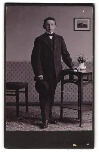 Fotografie Louis Schindhelm, Ebersbach i. S., Bürgerlicher Knabe im Anzug mit einer Fliege und dem Hut in der Hand