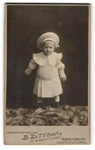 Fotografie B. Dittmar, Regensburg, Schäffnerstr. 104a, Kleines Kind im weissen Gewand mit einer weissen Mütze