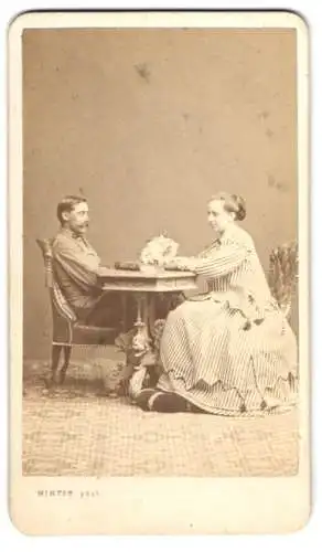 Fotografie M. L. Winter, Prag, K. u. K. Soldat in Uniform am Tisch mit seiner Frau im hellen gestreiften Kleid