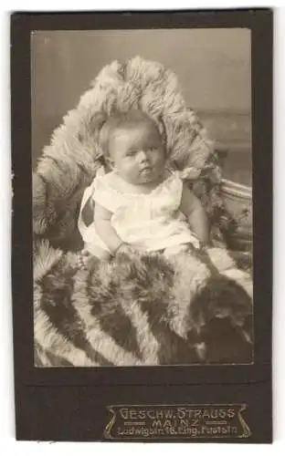 Fotografie Geschw. Strauss, Mainz, Ludwigstr. 16, Pausbäckiges Kleinkind im weissen Gewand auf einem Pelz