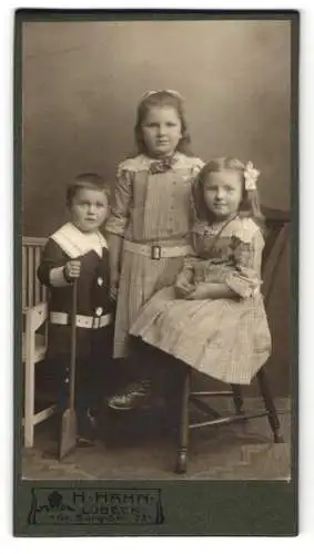 Fotografie H. Hahn, Lübeck, Gr. Burg-Str. 33, Junges Mädchen im karierten Kleid mit kleiner Schwester und kleinem Bruder
