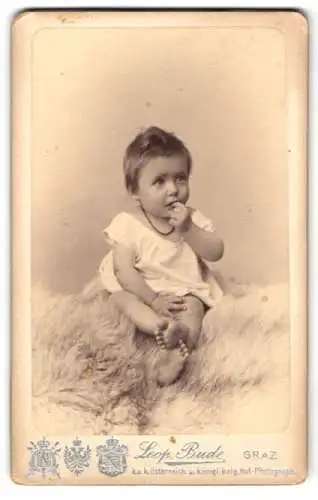 Fotografie Leopold Bude, Graz, Alleegasse 6 u. 8, Niedliches Kleinkind in weissem Kleid auf Fell