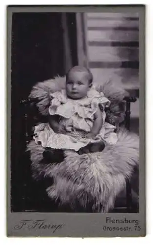 Fotografie F. Flarup, Flensburg, Grossestr. 75, Kleinkind mit grossen Augen im gestreiften Kleid auf einem Pelz