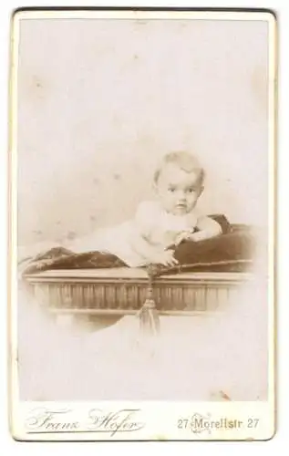 Fotografie Franz Hofer, Augsburg, Morellstr. 27, Kleinkind im weissen Gewand mit neugierigem Blick auf einem Kissen