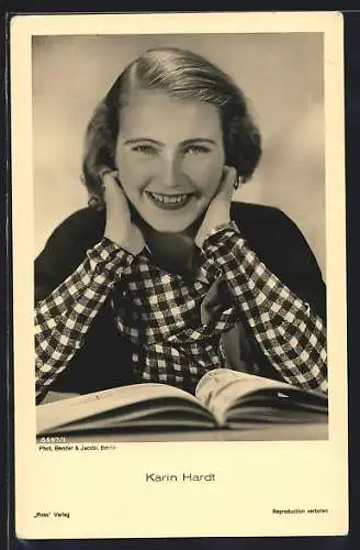 AK Schauspielerin Karin Hardt lächelnd am Tisch vor einem Buch sitzend