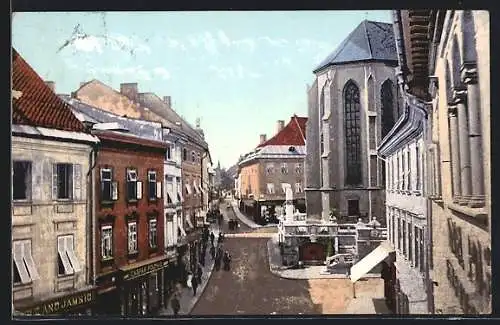 AK Villach, Schulstrasse mit Geschäften und Kirche
