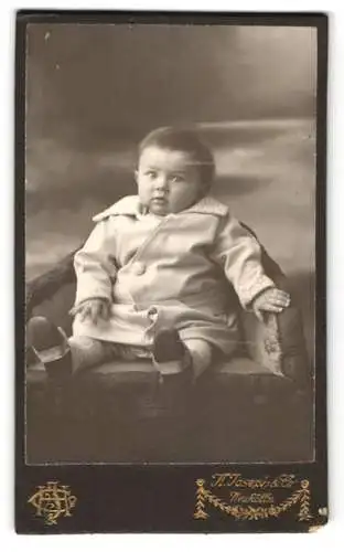 Fotografie K. Joseph & Co., Neukölln, Süsses Baby sitzend im weissen Mantel