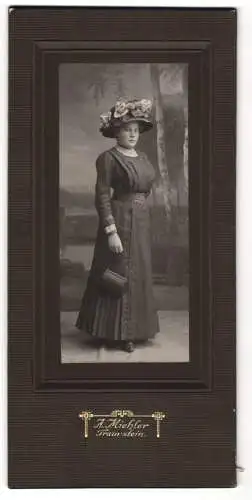 Fotografie A. Miehler, Traunstein, Junge Dame im taillierten Kleid mit Handtasche und floral verziertem Hut