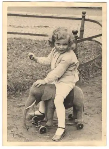Fotografie Spielzeug, blondes Mädchen reitet auf Stoff-Elefant mit Rädern