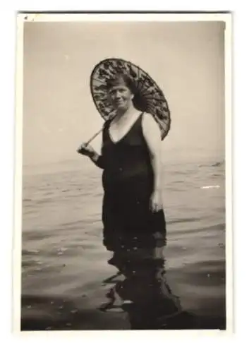 Fotografie unbekannter Fotograf und Ort, Frau im Badeanzug mit Badehaube und Schirm stehend im Wasser