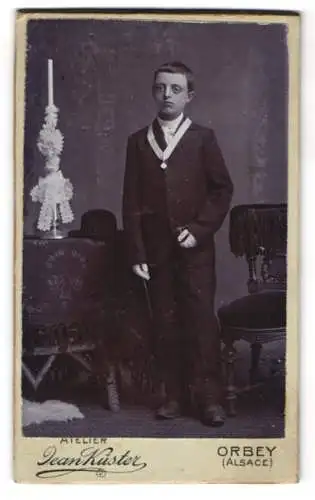Fotografie Jeans Küster, Orbey, junger Knabe im Anzug mit Halsband zu seiner Kommunion
