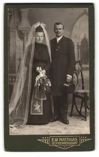 Fotografie E. W. Matthias, Seifhennersdorf, sächsisches Brautpaar im schwarzen Hochzeitskleid und Anzug, Zylinder