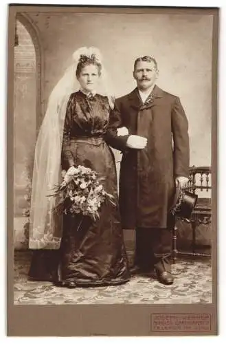 Fotografie Joseph Werner, München, Brautpaar im schwarzen Hochzeitskleid und Anzug, geschmückter Zylinder