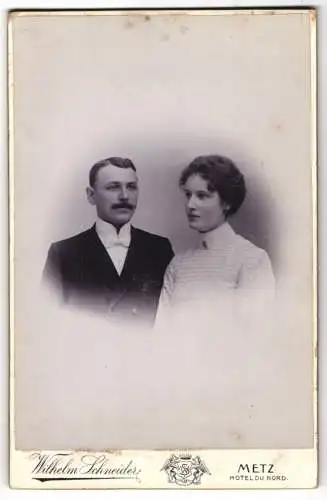Fotografie Wilhelm Schneider, Metz, Junges Ehepaar, er im Anzug mit weisser Fliege, sie im Kleid mit Zierfalten
