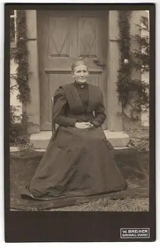 Fotografie W. Breiner, Gronau /Hann., Ältere Dame im langen, taillierten Kleid vor ihrer Haustür sitzend