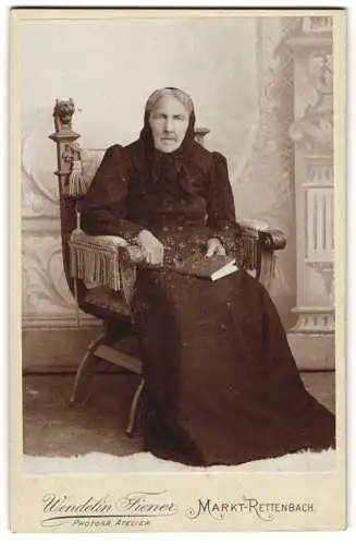 Fotografie Wendelin Fiener, Markt-Rettenbach, Alte bürgerliche Dame mit Kopftuch auf einem Stuhl, mit einem Buch
