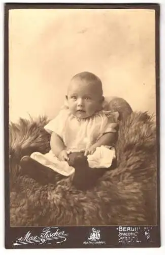 Fotografie Max Fischer, Berlin, Invalidenstr. 164, Niedliches Kleinkind im Kleid sitzt auf Fell