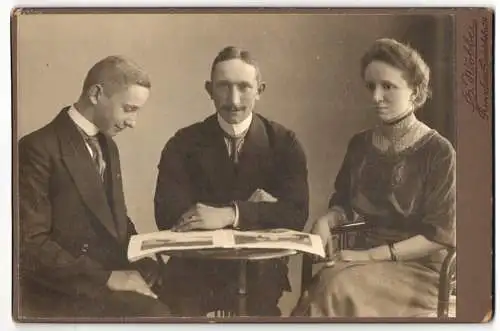 Fotografie E. Wobber, Prenzlau, Friedrichstr. 215, Junge Frau im Kleid und Zwei Herren mit Zeitung am Tisch