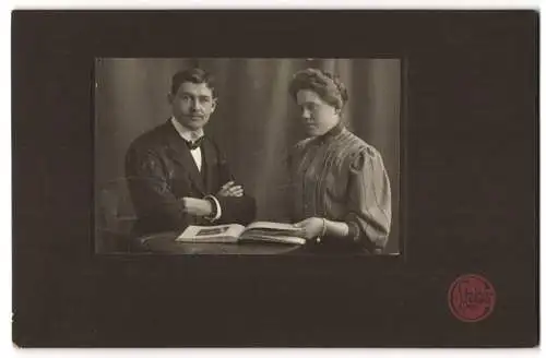 Fotografie Steiger, Moers, Elegant gekleidetes Paar mit Album am Tisch
