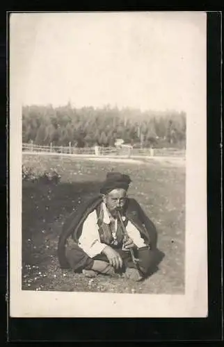 AK Älterer Mann in Nationaltracht raucht Pfeife auf einer Wiese