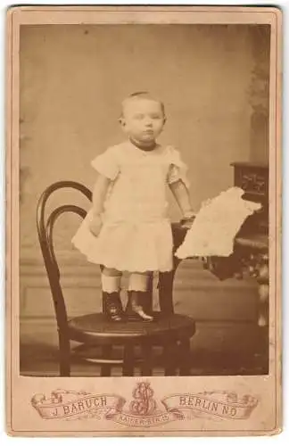 Fotografie J. Baruch, Berlin, Kaiser-Strasse 15, Kleinkind mit Kurzhaarfrisur im Kleidchen auf einem Stuhl